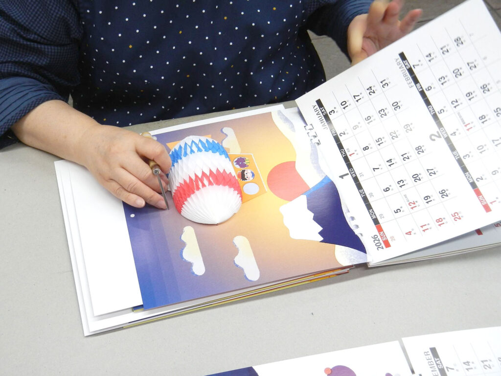 手仕事でひとつひとつ取り付けされてます　ハニカムカレンダー・ポップアップカレンダー2025 株式会社エクセルポイント